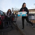 Cascade High senior Katerina Freeman uses her foot to stop a runaway cart as she and Mariana Cardona load up a Mini Cooper with food as students, alumni and volunteers gather and deliver food from Cascade High School on Wednesday, Dec. 14, 2016 in Everett, Wa. (Andy Bronson / The Herald)