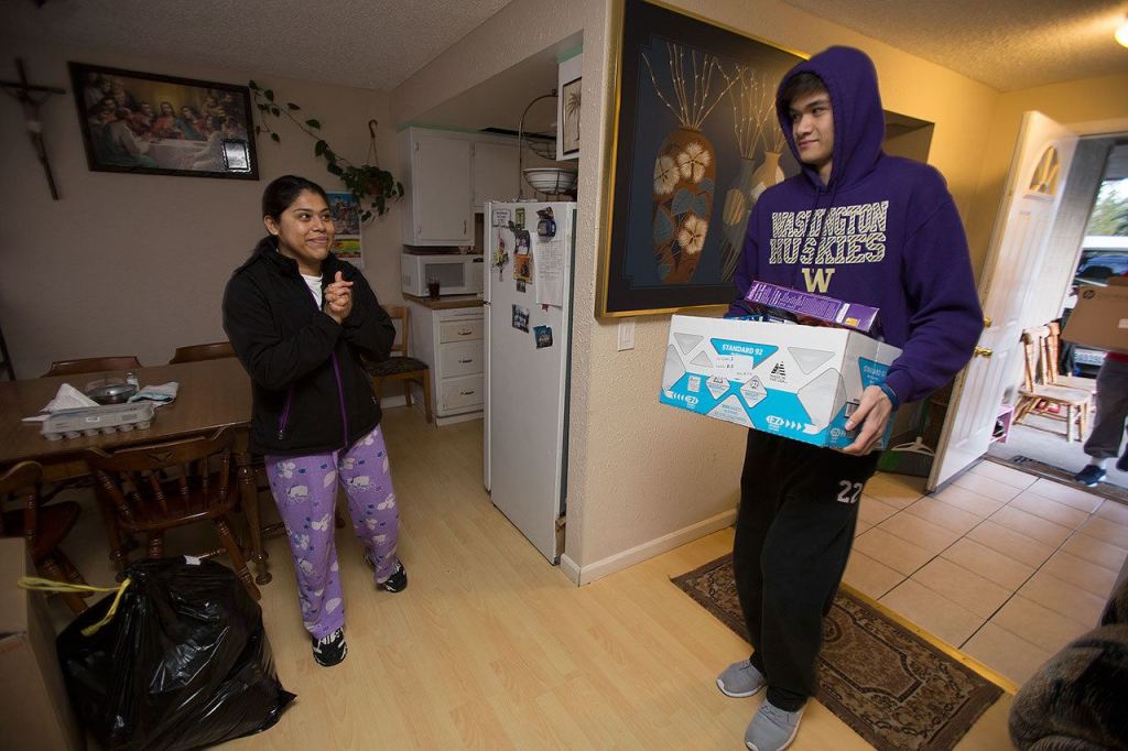 Rosa Garcia smiles as Cascade High senior Briar Nguyen carries in one of several boxes of food for the family as students, alumni and volunteers gather and deliver food from Cascade High School on Wednesday, Dec. 14, 2016 in Everett, Wa. (Andy Bronson / The Herald)