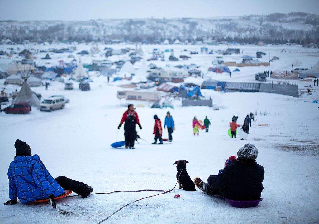 The Oceti Sakowin camp where people have gathered to protest the Dakota Access oil pipeline stands in the background as a children sled down a hill in Cannon Ball, North Dakota, on Thursday, Dec. 1. (AP Photo/David Goldman)