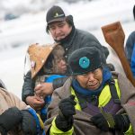 In this Thursday, Dec. 1, photo, Patty Sam Porter of Colville, Washington, right, cries after reaching shore by canoe with fellow members of the Colville Confederated Tribes, J.P. Pacodas, left, and Virginia Redstar, rear, at the Oceti Sakowin camp where people have gathered to protest the Dakota Access oil pipeline in Cannon Ball, North Dakota. The women traveled from Montana with fellow tribal members on canoe for 10 days down the Missouri river to reach the camp. (AP Photo/David Goldman)
