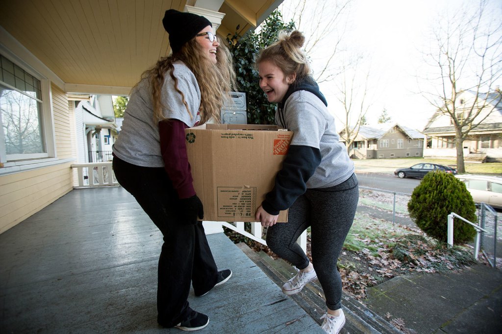 Hope Peterson, left, ad Katie Helmke, right, laughs as they struggle to carry a box of food up steps as they deliver food to a needy family from Cascade High School on Wednesday, Dec. 14, 2016 in Everett, Wa. (Andy Bronson / The Herald)