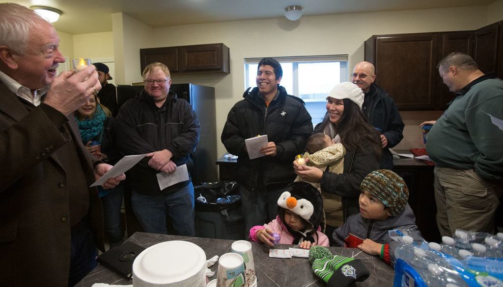 Pastor Ken Long holds an electric candle as he blesses the new house from Habitat for Humanity of Snohomish County for Ray and Sandy Flores (center) on Saturday. The previous house on the site burned down in 2014, and Long didn&rsquo;t want to use &rdquo;real fire&rdquo; in the new home. (Andy Bronson / The Herald)