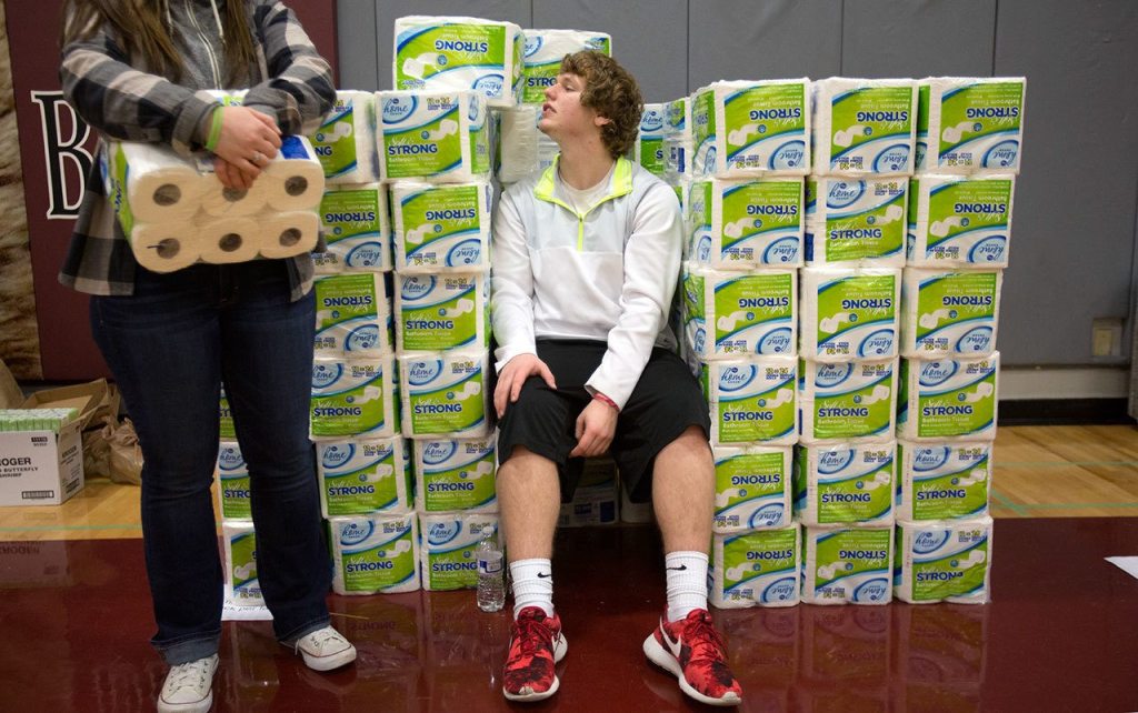 Sam Barnes peers over wall of toilet paper rolls as he and Katrina Bishop wait to hand them out to students, alumni and volunteers gathering and delivering food and other items from Cascade High School on Wednesday, Dec. 14, 2016 in Everett, Wa. (Andy Bronson / The Herald)