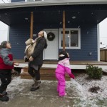 With her infant son Matias on her chest, Sandy Flores enjoys snow falling with her son Ray J. and daughter Sasha in front of their new home on Dec. 17, 2016, in Everett. Flores, her husband, Ray, and their three young kids became the new owners of Phoenix II, a house in North Everett from Habitat for Humanity of Snohomish County and for which they contributed over 500 hours of sweat equity in the construction of the home. (Andy Bronson / The Herald)