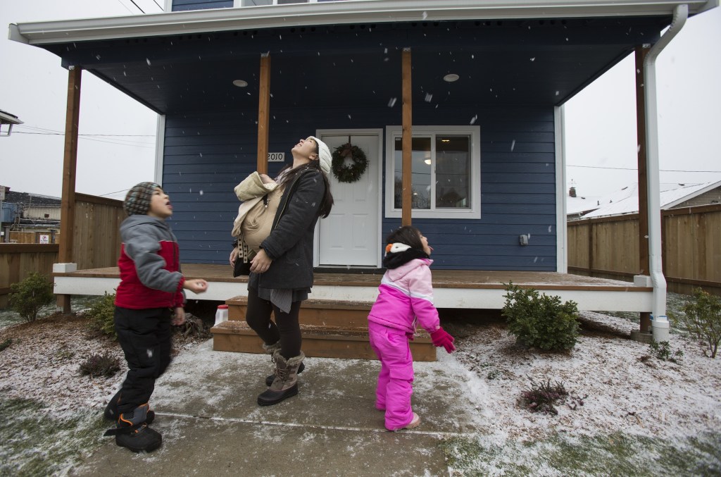 With her infant son Matias on her chest, Sandy Flores enjoys snow falling with her son Ray J. and daughter Sasha in front of their new home on Dec. 17, 2016, in Everett. Flores, her husband, Ray, and their three young kids became the new owners of Phoenix II, a house in North Everett from Habitat for Humanity of Snohomish County and for which they contributed over 500 hours of sweat equity in the construction of the home. (Andy Bronson / The Herald)