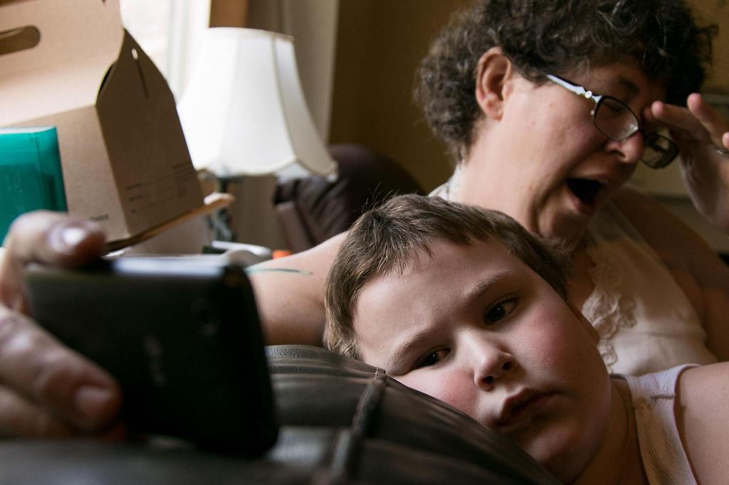 Cheryl Pyles holds her phone while her son Jessie Pyles, 7, watches a video during down time at their home in Lake Stevens. Raising Jessie, who has autism with developmental delay, a sensory - processing disorder and various other medical conditions, a labor of love with often one step forward and two steps back. (Kevin Clark / The Herald)