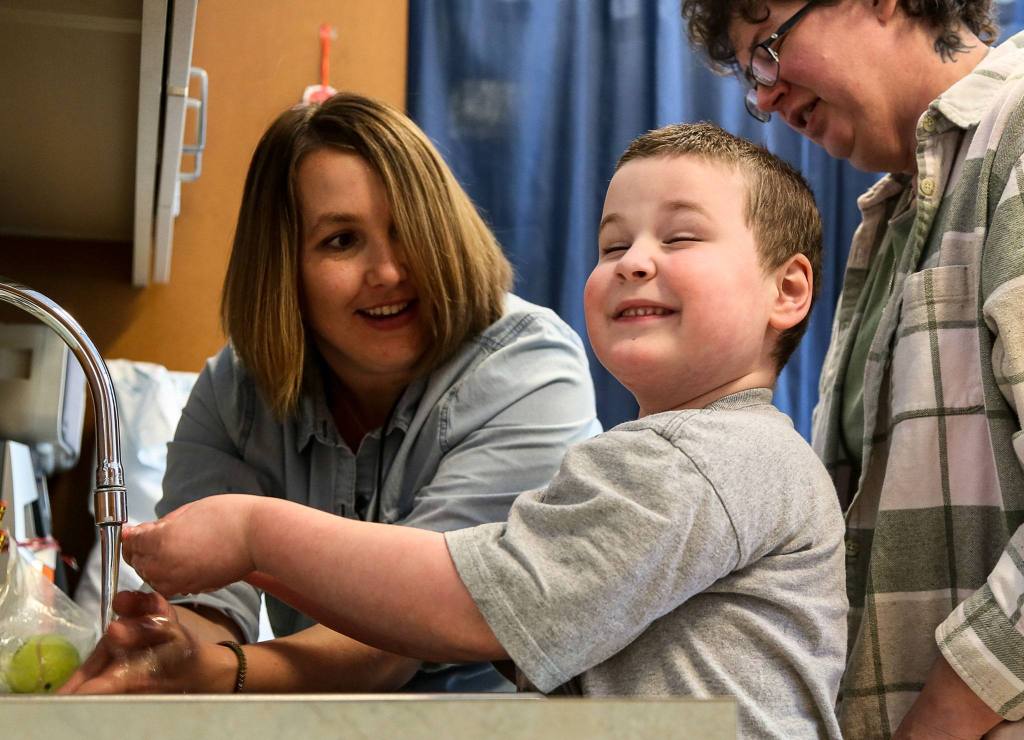 Katie Dawson, occupational therapist, coaches Jessie to wash his hands with Cheryl Pyles, Jessie&rsquo;s mother, looking on at the Providence Children&rsquo;s Center in Everett. The sessions coach Jessie on hand-eye coordination, washing hands, putting on socks and shoes and much more. (Kevin Clark / The Herald)