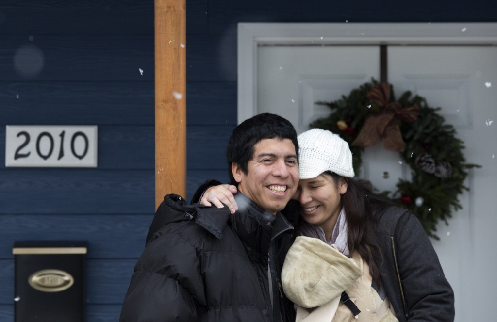 Ray and Sandy Flores hug on their front porch after accepting the keys, earlier that morning, to their new home from Habitat for Humanity of Snohomish County on Saturday, Dec. 17, 2016 in Everett. The Flores and their three young kids became the new owners of Phoenix II, a house in North Everett, which they contributed over 500 hours of sweat equity in its construction. (Andy Bronson / The Herald)