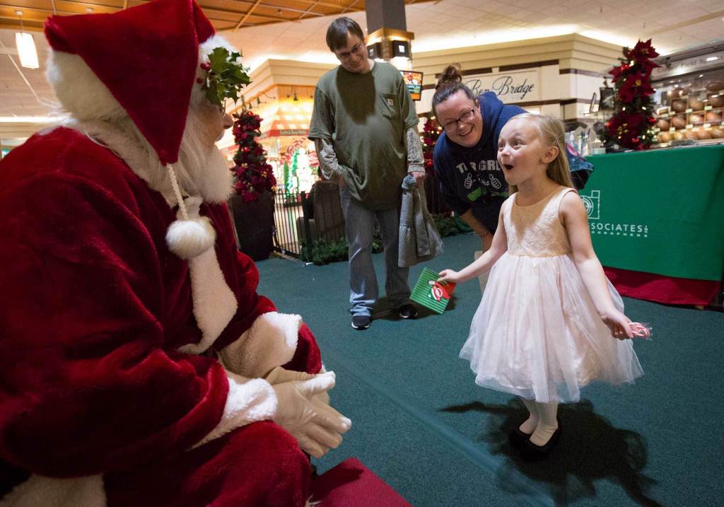 Kloe Gregory, 4, reacts with excitement with her parents Matt and Khyrsha Gregory while talking with Santa, 74-year-old Tom LaBelle, in the Everett Mall on Nov. 28. LaBelle began wearing the suit after his wife suggested he try it out. He&rsquo;s now a regular each year as a mall Santa and has an entire collection of answers about Santa&rsquo;s duties for his most inquisitive visitors. (Daniella Beccaria / The Herald)