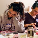 Ella Estlund (left) writes with tiny letters in the spaces around graphic designs she created using a fine-point pen. Cynthia Gahan uses rubber stamps to apply the letters of words in her journal. (Dan Bates / The Herald)