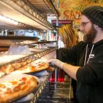 Joe Jarvis retrieves a slice to warm at Brooklyn Bros. Pizzeria at the downtown Everett shop. Brooklyn Bros. sells pizza by the slice or by whole. (Kevin Clark / The Herald)