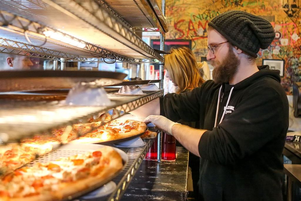 Joe Jarvis retrieves a slice to warm at Brooklyn Bros. Pizzeria at the downtown Everett shop. Brooklyn Bros. sells pizza by the slice or by whole. (Kevin Clark / The Herald)