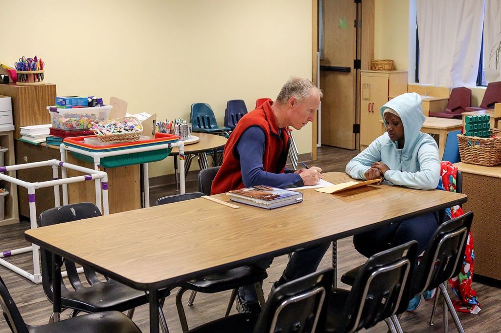 Dirk Howe (left) helps Aline Mumararungu with school work at Trinity Lutheran Church in Lynnwood on Jan. 7. (Kevin Clark / The Herald)