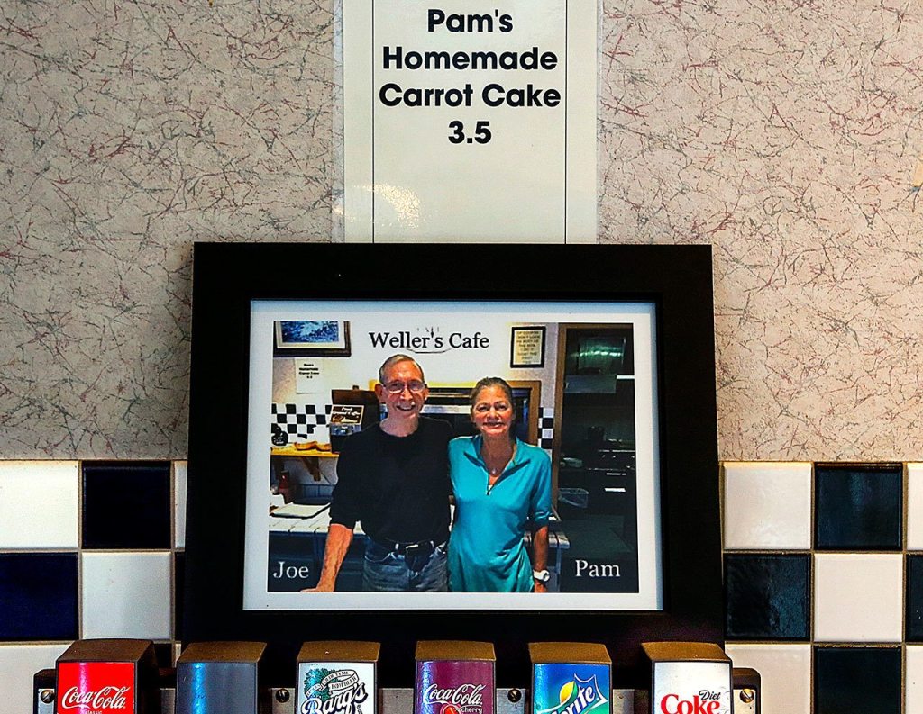 A picture of Joe and Pam Weller hangs just above the soda fountain and just below the Pam&rsquo;s Homemade Carrot Cake sign. (Dan Bates / The Herald)