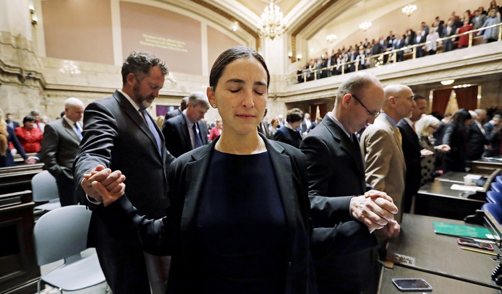 Sen. Rebecca Saldana, D-Seattle (center), holds hands with fellow legislators during an opening invocation at a joint session of the Legislature on Wednesday, Jan. 11, in Olympia. (AP Photo/Elaine Thompson)