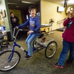 Quinn Schmitz, 11, rides her new adaptive tricycle while her grandmother Anita Kerwood (right), her grandfather Craig Kerwood (center left) and other family members and physical therapists applaud at ATI Physical Therapy in Everett. The ATI Foundation helps children with disabilities and presented Schmitz with the tricycle as a surprise. (Daniella Beccaria / The Herald)