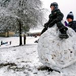 At the popular park outside Mount Pilchuck Elementary School in Lake Stevens, where they would normally be in class, kindergarten student James Eichert, 6, sits atop a huge snowball while first-grader Mason Jones, 7, packs more snow around him Monday morning. (Dan Bates / The Herald)