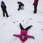 Rada Anderson, 3, makes a snow angel while her brother, Declan Anderson, 5, and parents Chris and Erin Anderson build a snowman at College Place Middle School on Monday in Lynnwood. (Daniella Beccaria / The Herald)