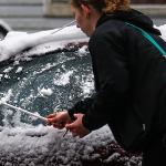 Having tried a piece of cardboard, Hanna Weaver uses a coat hanger to remove snow and ice from her car in north Everett early Monday. (Dan Bates / The Herald)