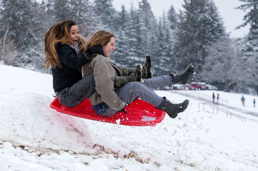 Kaitlyn Nguyen (left) and Grace McCullough scream as they hit a jump while sledding at Stanwood High School on Monday. (Andy Bronson / The Herald)