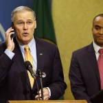 Washington Gov. Jay Inslee briefly speaks into his phone after it rang during a news conference, Thursday, Feb. 23, at the Capitol in Olympia, as general counsel Nick Brown looks on at right. (AP Photo/Ted S. Warren)