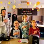 Dressed for a big day of space exploration, Highland Elementary principal Ryan Henderson enlists (from left) third-grader Harmony Piffath, second-grader Camrie Ingram and third-grader Makayla Goshorn to help lead the pledge. (Dan Bates / The Herald)