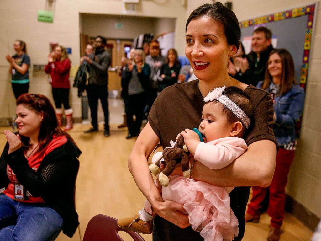 While Jerome Aparis finishes his presentation and gathers his gear, his wife, Lea Aparis, and daughter, 9-month-old Malaya, watch from a corner of the Emerson Elementary gymnasium. (Dan Bates / The Herald)