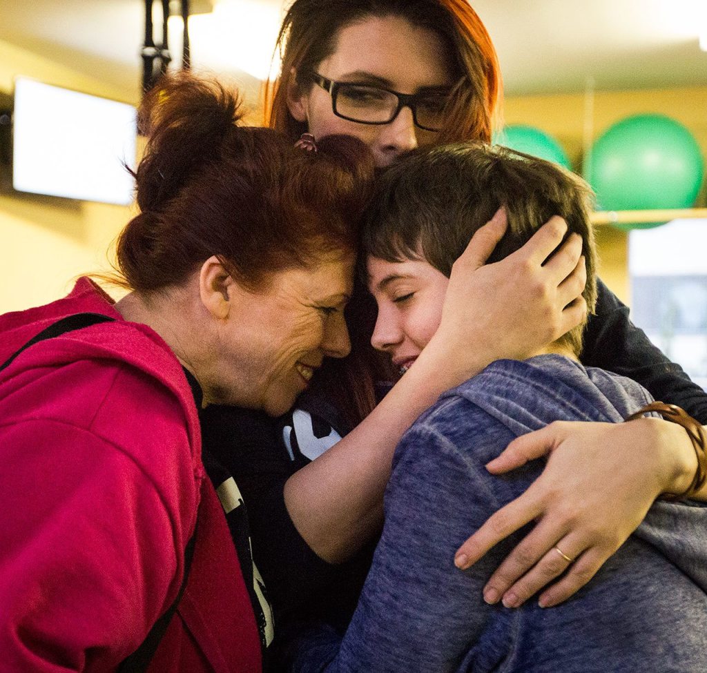Eleven-year-old Quinn Schmitz shares a moment with her mom, Sarah Blakeley, and her grandmother, Anita Kerwood, at ATI Physical Therapy on Thursday in Everett. The ATI Foundation surprised Schmitz with a new tricycle in front of her family, friends and physical therapists. (Daniella Beccaria / The Herald)