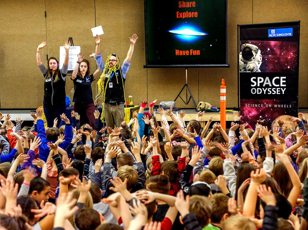 Entertaining educators from Pacific Science Center, Janice Crew (left) Kate Wellens and Mike Sweeney get a lot of small hands at the end of their presentation to all the second-graders at Highland Elementary in Lake Stevens on Thursday. (Dan Bates / The Herald)