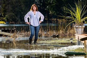 Debbie Bly-Olsen stands in her flooded yard as one of two sump pumps sprays water back into the yard on Lake Serene on Wednesday, Feb. 1, 2017 in Lynnwood, Wa. Bly-Olsen says she and her husband have gone through three pumps since the flooding started. And the water is already threatening to leak through the two-foot wall built by the previous owner to deal with high water. (Andy Bronson / The Herald)