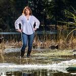 Debbie Bly-Olsen stands in her flooded yard as one of two sump pumps sprays water back into the yard on Lake Serene on Feb. 1 in Lynnwood. (Andy Bronson / Herald file)