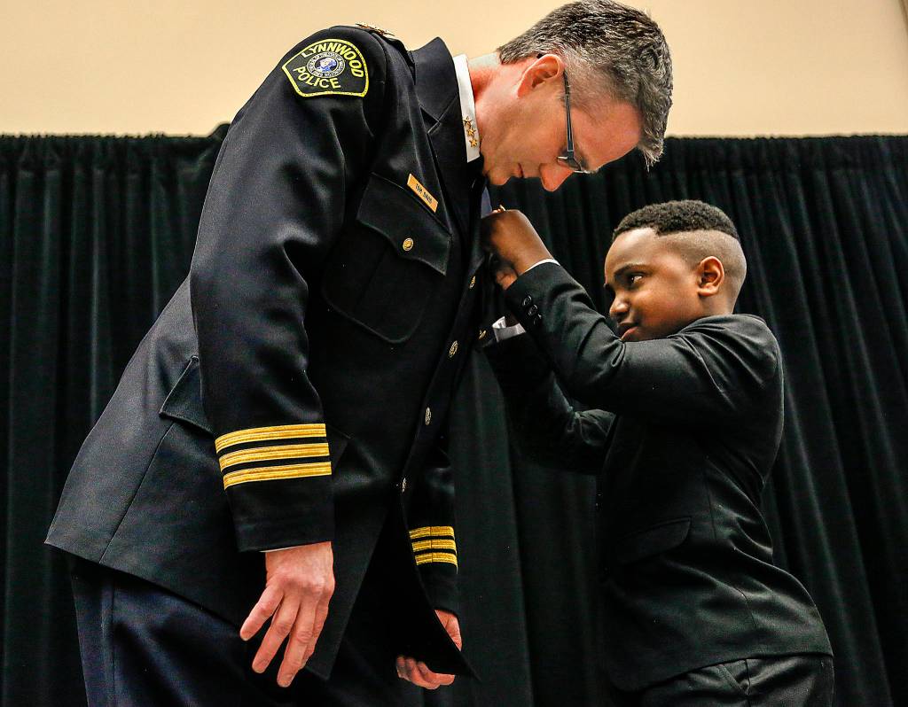 Tyson Webster, 9, of Shoreline, pins a badge on Lynnwood&rsquo;s new Chief of Police Tom Davis on Tuesday, April 25, at the Lynnwood Convention Center. (Dan Bates / The Herald)