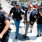 Alex Jones (center-right) is escorted by police out of a crowd of protesters outside the Republican convention in Cleveland last summer. (AP Photo/John Minchillo, File)