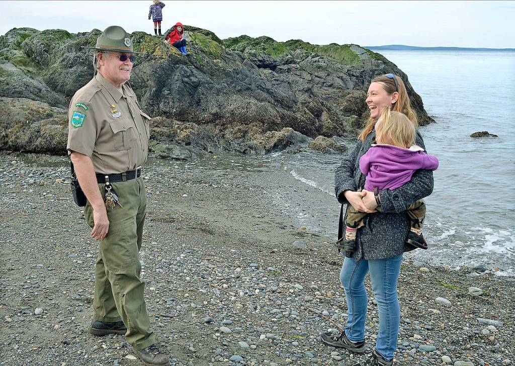 Retiring assistant park manager at Deception Pass State Park Rick Blank talks to visitor Brianna Lyon, holding her youngest child, Kestrel, at West Beach on March 20. Blank has been an employee of Washington State Parks for 45 years and is the longest-tenured ranger in the field. He arrived at Deception Pass in 1990. (Scott Terrell/Skagit Valley Herald via AP)