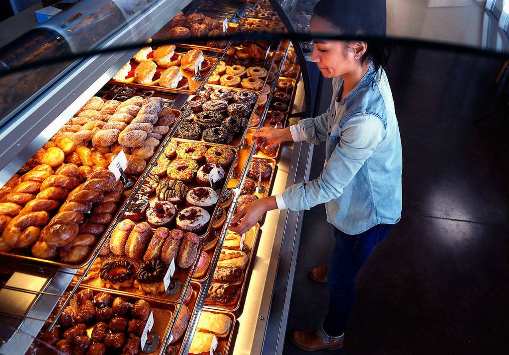 Melissa Despi restocks displays, including those containing some of their American-style doughnuts, at the customer service counter. (Dan Bates / The Herald)