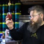 Erik Newquist, owner and brewer at Aesir Meadery, looks at a glass of blackberry mead before tasting it at his shop in Everett. (Andy Bronson / The Herald)