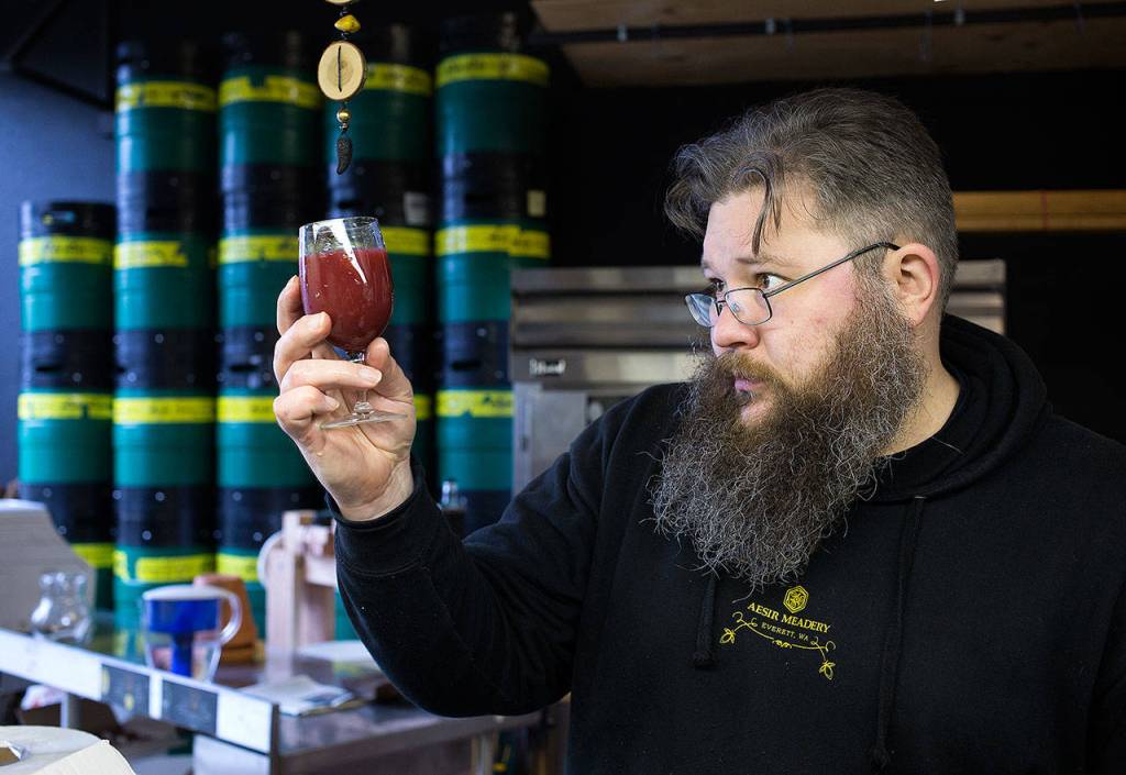 Erik Newquist, owner and brewer at Aesir Meadery, looks at a glass of blackberry mead before tasting it at his shop in Everett. (Andy Bronson / The Herald)