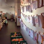 Melissa Despi restocks displays between customers. On the wall behind the counter, dozens of drawings by children, who created them using the color crayons and paper set out by Despi, who says she loves children&rsquo;s art. Dan Bates / The Herald)