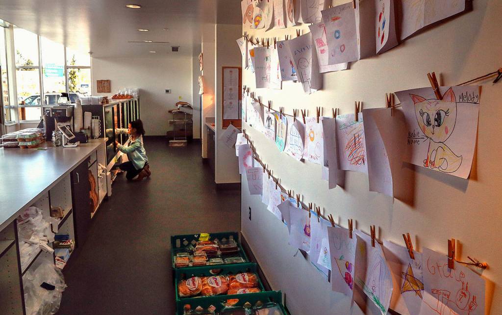 Melissa Despi restocks displays between customers. On the wall behind the counter, dozens of drawings by children, who created them using the color crayons and paper set out by Despi, who says she loves children&rsquo;s art. Dan Bates / The Herald)