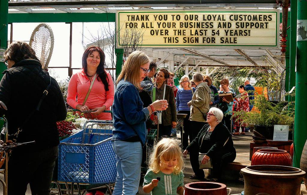 A sign near the back of one of three long lines to check out stands at Wight&rsquo;s Home & Garden sale, Friday, carries a message of thanks to longtime customers&mdash;with an unusual sign-off. Customers nearest are Judy Hobert (far left) Oksana Donskoy (pink) Martha Overland and her grandaughter Isabelle Strandy, 2, and Ellie Norsworthy-Tingley (sitting). (Dan Bates / The Herald)