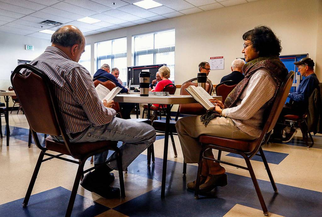 Husband and wife Hemant (left) and Mamta Shah read while waiting to enter a duplicate bridge game by way of rotation, due in part to the lower numbers of players available and needing an even four players per table. (Dan Bates / The Herald)