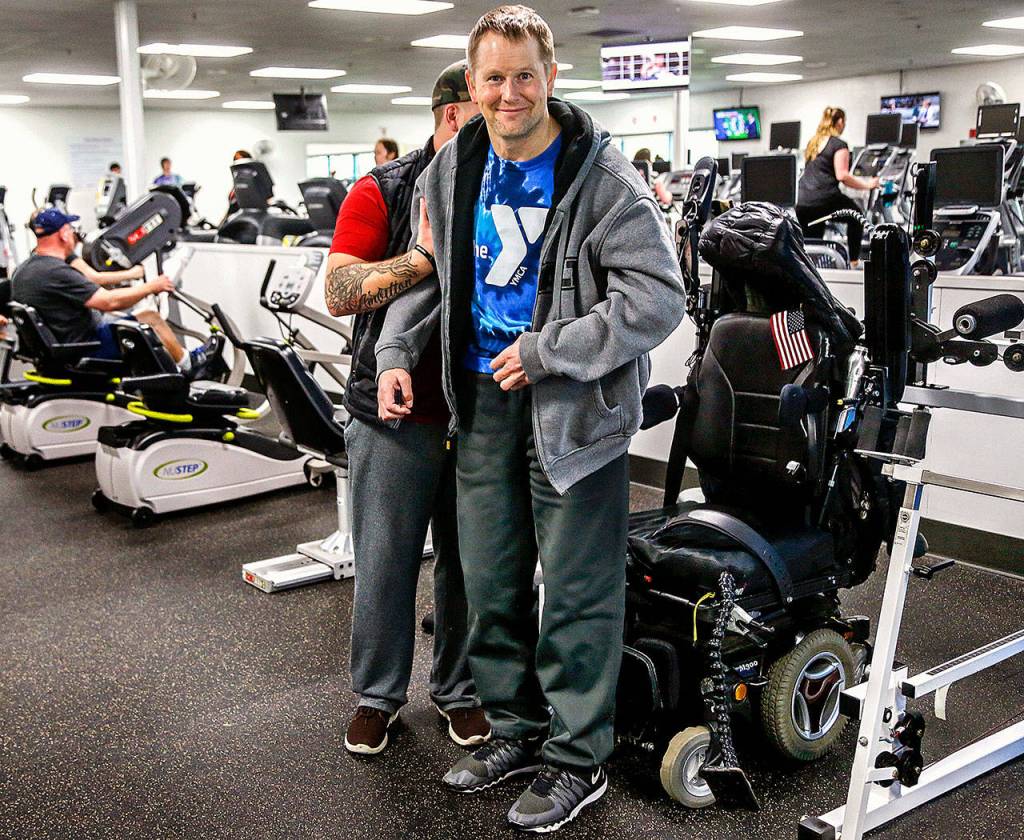 With help from his assistant Duitsman stands up from his wheelchair after exercising on special equipment Wednesday at the Marysville YMCA. (Dan Bates / The Herald)