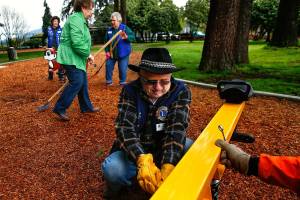 Lions Club volunteer Roy Johnson (center) gets some help tightening spring mounting bolts on a play structure from Ray Drake (right), who is with Arlington Maintenance and Operations, earlier this week. Other Lions volunteers Maxine Jenft (green), local Lions President Joan Flesher (back left) and 40-year member Donna Knight tidy up the bark as they near completion of their work on a new children&rsquo;s playground at Terrace Park in Arlington. (Dan Bates / The Herald)