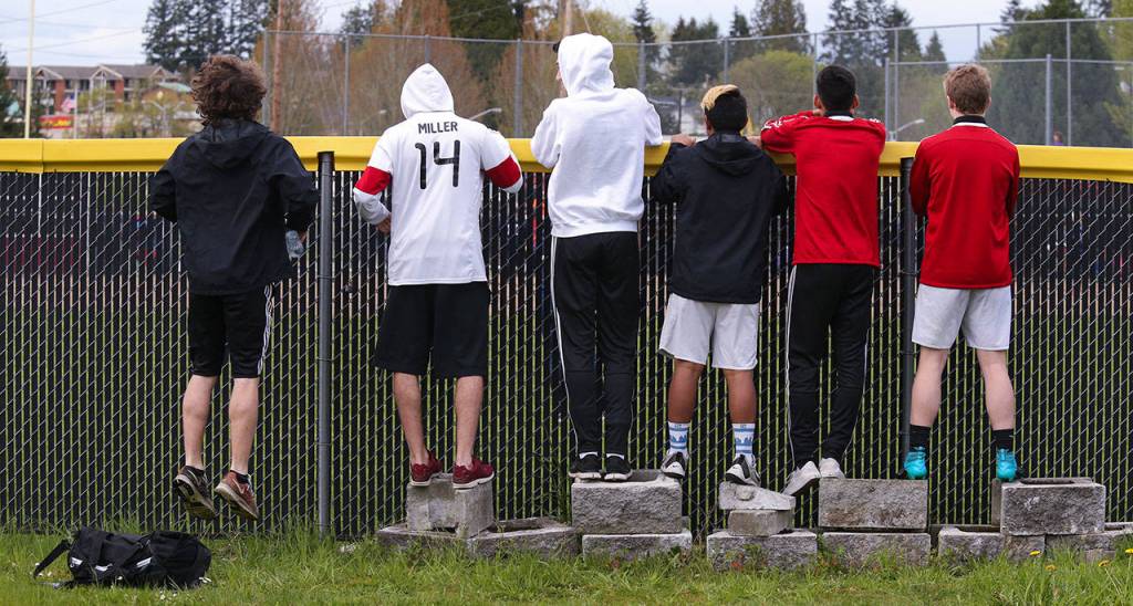 Snohomish junior Bohdi Uderitz (left) leaps up and down to see over the outfield wall as spectators watch a softball game between Snohomish and Meadowdale on April 25 in Snohomish. (Andy Bronson / The Herald)