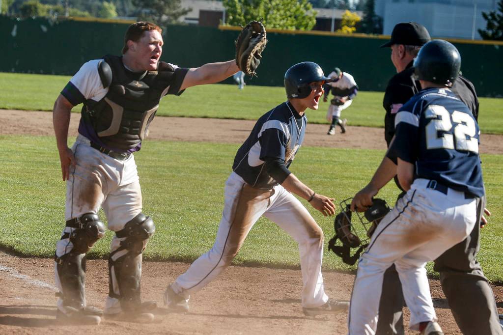 Edmonds-Woodway catcher Garrison Krohn (left) looks for a call from the umpire as Arlington&rsquo;s Trevor Kazen (center) slides in safely to home plate during a 3A state playoff game on May 20, 2017, at Dream Field in Mount Vernon. (Ian Terry / The Herald)