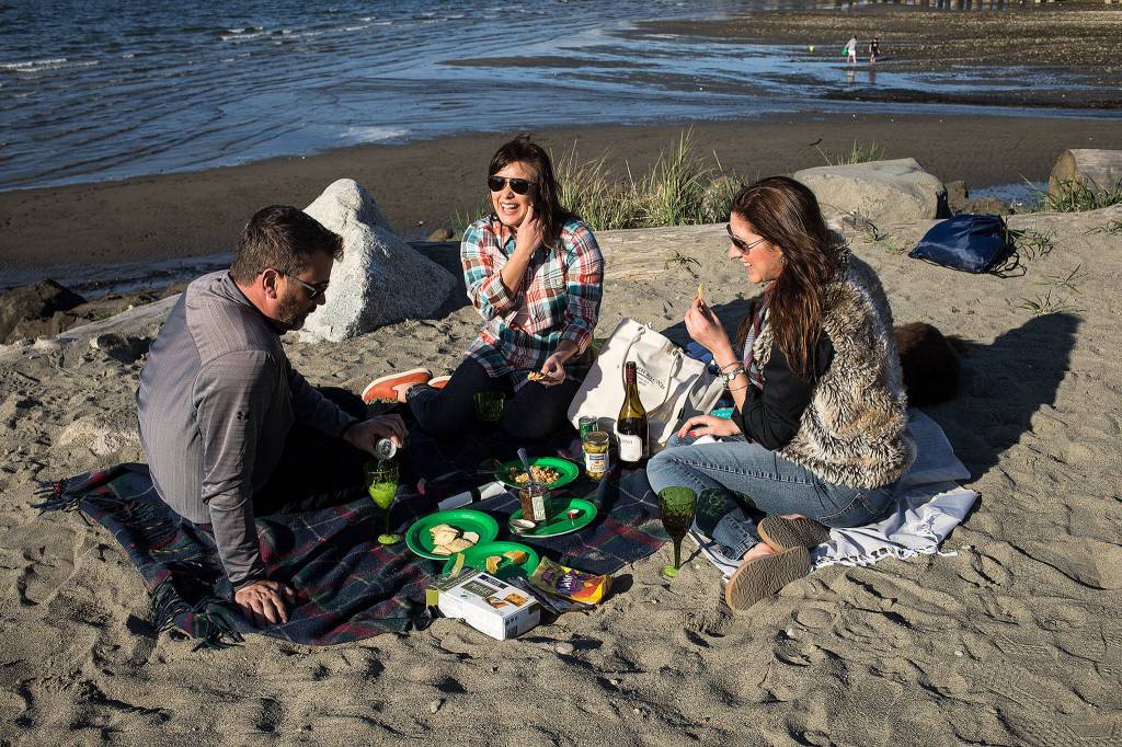 Andrew Gaston, Julissa Downing, and Kelly Colman enjoy a picnic at Edgewater Beach in Mukilteo. Colman owns Proper Picnic, a company that sells ready-to-go picnics. (Andy Bronson / The Herald)