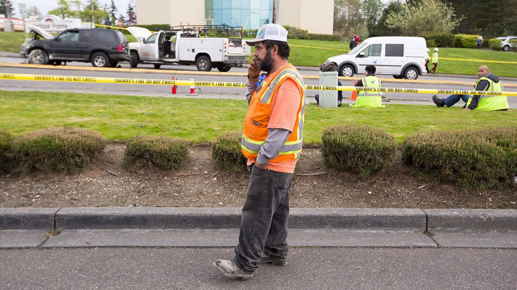 Juan Teran talks on the phone as he waits for his work truck (second from left) to be released from the scene of the plane crash Tuesday in Mukilteo. Burning fuel landed on his truck as he waited for the light at the intersection of Harbour Pointe Boulevard SW and the Mukilteo Speedway.(Andy Bronson / The Herald)