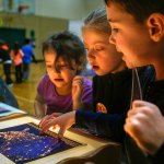 From left, Highland Elementary School first-graders Cheyenne Hampton, Addison Vaule and Alden Jordan enjoy viewing photographic transparencies taken from space at one of many displays brought into the school in February by Pacific Science Center&rsquo;s Science on Wheel&rsquo;s program. The school recently was honored as a Lighthouse School for raising student leaders. (Herald file photo by Dan Bates)