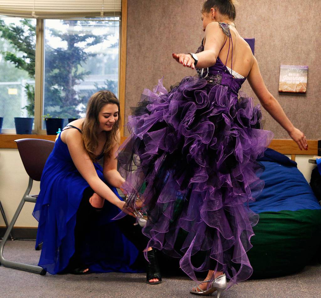 IzSabella Haviland, 17, slips a shoe, Cinderella-style, on her friend Tetyana Popach, 17, while trying on formal wear to wear Friday night to their school&rsquo;s first-ever prom. (Dan Bates / The Herald)
