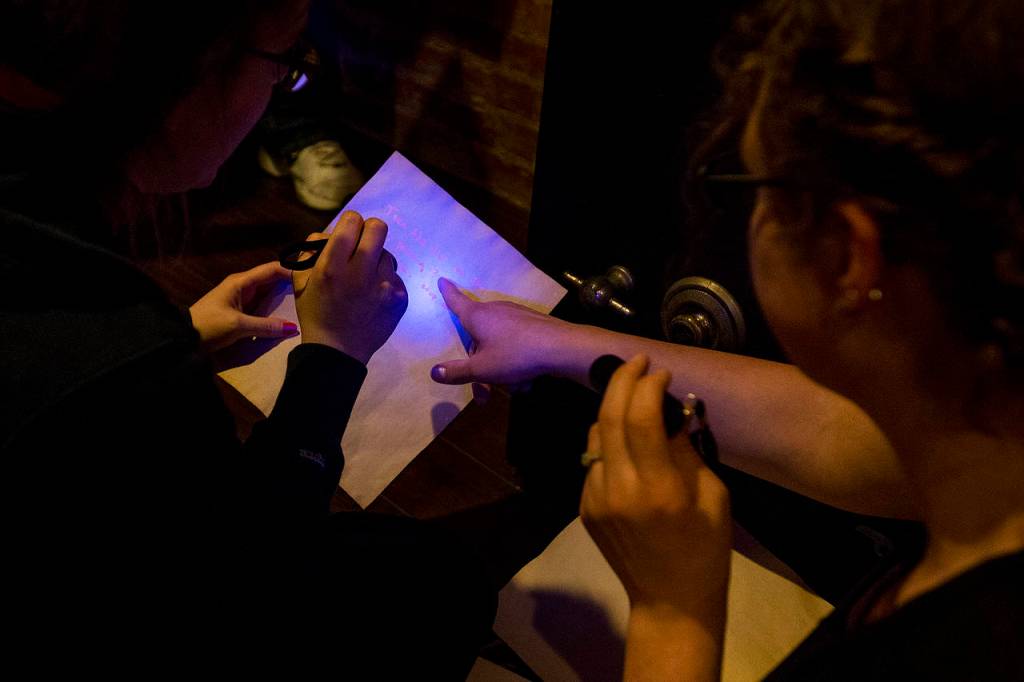 Catherine Harlow (left) and Alicia Flansburg use blacklights to find hidden messages on documents at the new Escape Scene in downtown Everett on May 6. (Ian Terry / The Herald)